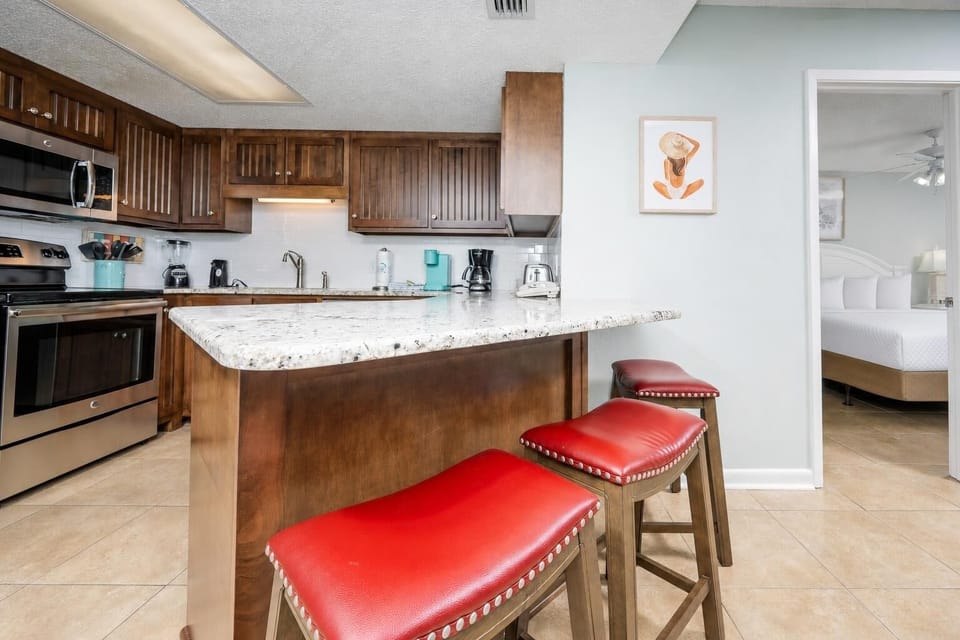 Warm wooden cabinets and red bar stools complement the granite breakfast bar in this inviting kitchen space