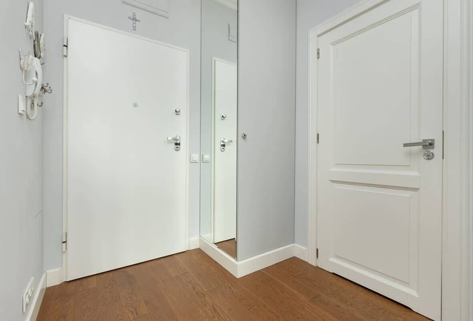 A hallway with white doors, wooden flooring, and a mounted coat rack.
