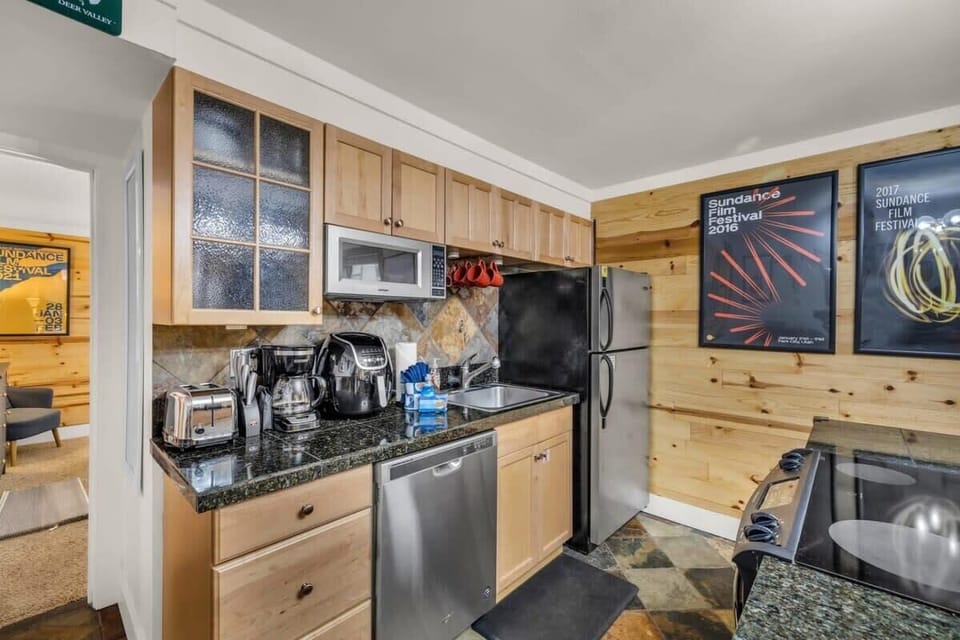 The kitchen is fully equipped with high-end stainless steel appliances, granite countertops, stone tile floors, and a stylish lighting fixture.