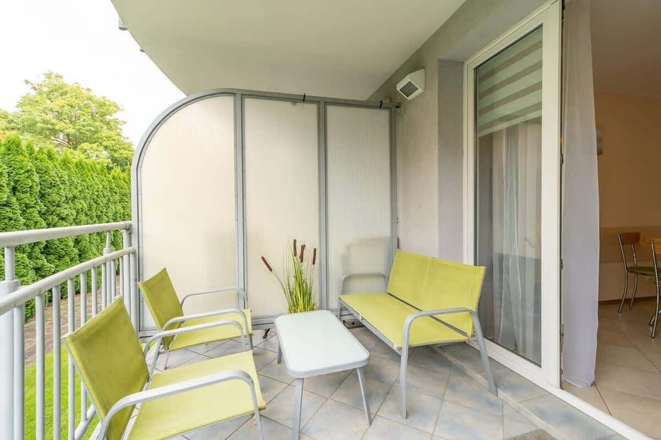 A cozy balcony setup with green chairs, a small table, and decorative plants.








