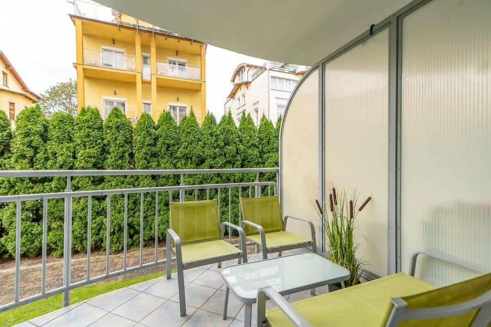 A balcony view featuring outdoor seating, green accents, and a surrounding privacy hedge.

