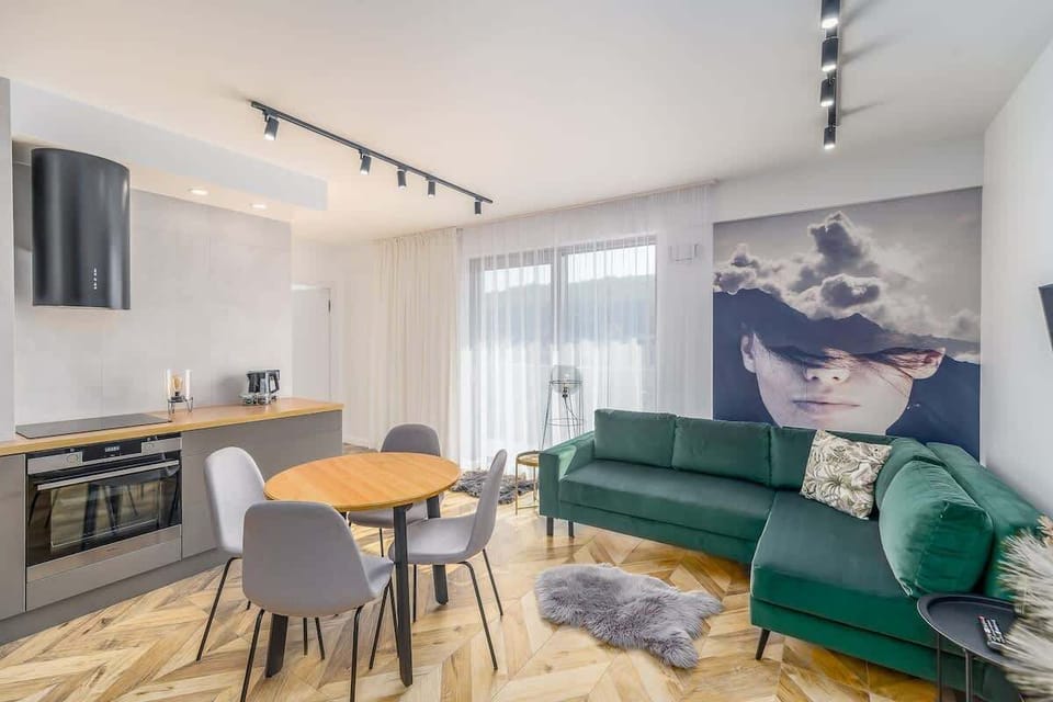 A wide shot of the living room and kitchen, highlighting the green sofa, the round dining table, and the mural on the wall.
