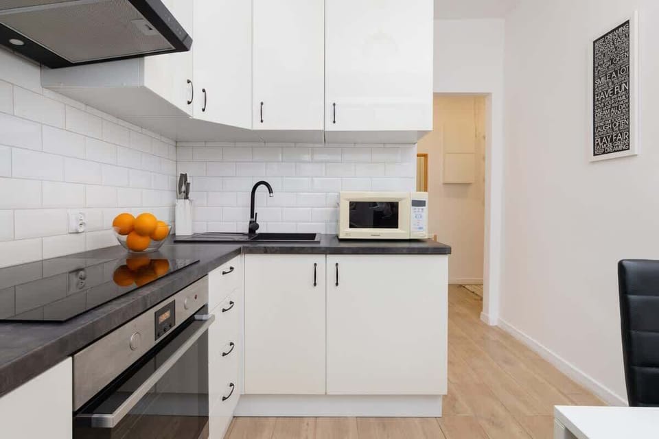 A modern kitchen with white cabinets, black countertops, a microwave, and wooden flooring.
