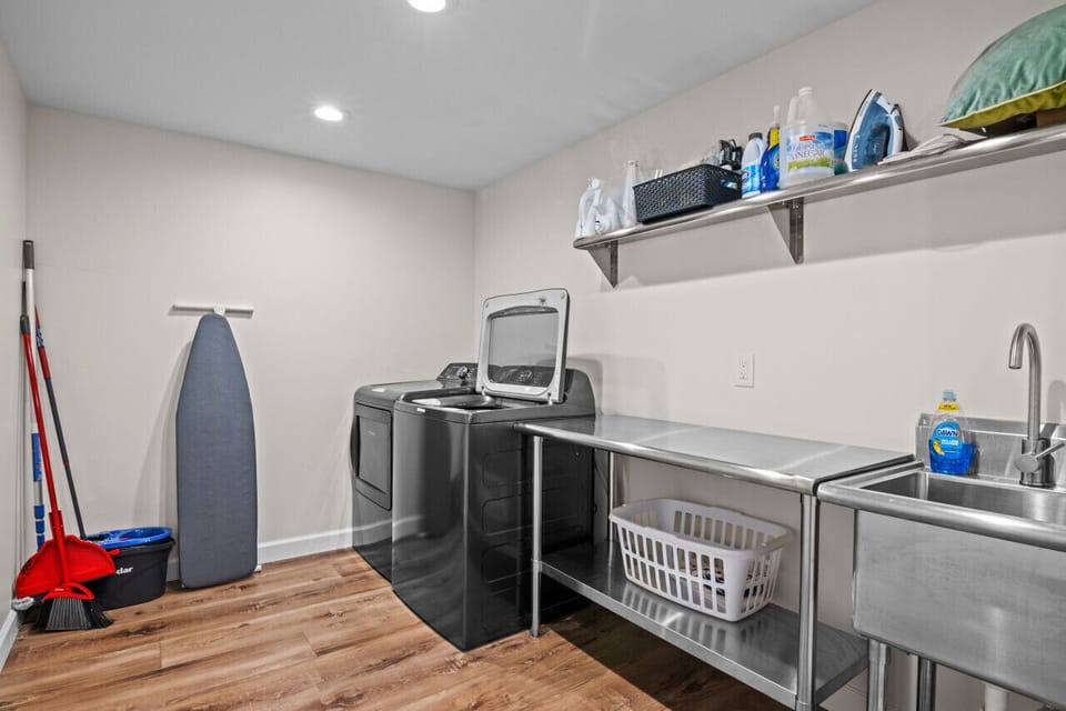 Laundry room with stainless steel utility sink, ironing board, and cleaning supplies.