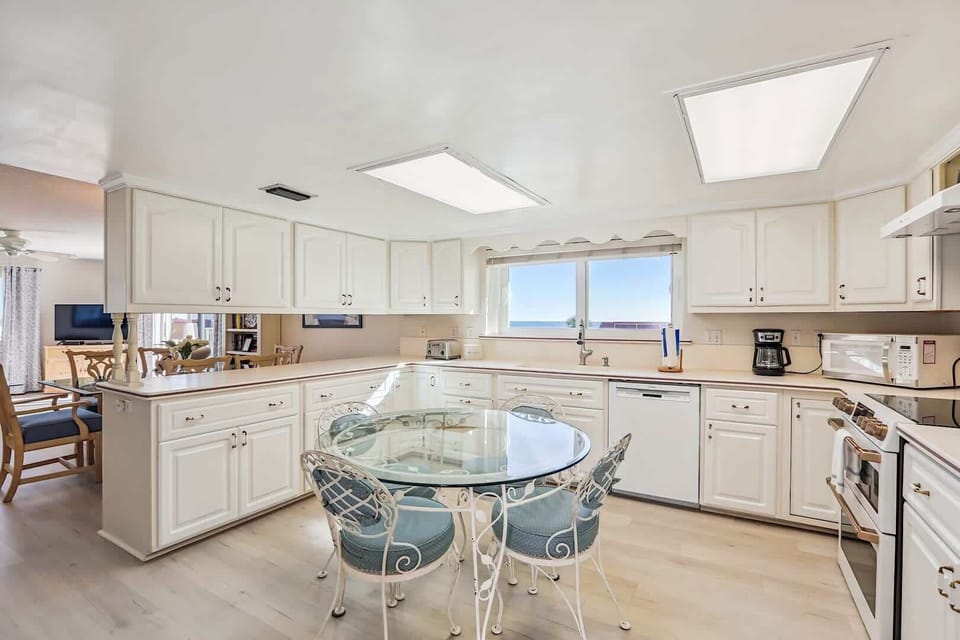 - Spacious kitchen with white cabinets modern appliances and ocean view window  
- Glass dining table with seating makes meal times simple for groups and families  
- Fully stocked with everything needed to cook during your vacation stay  