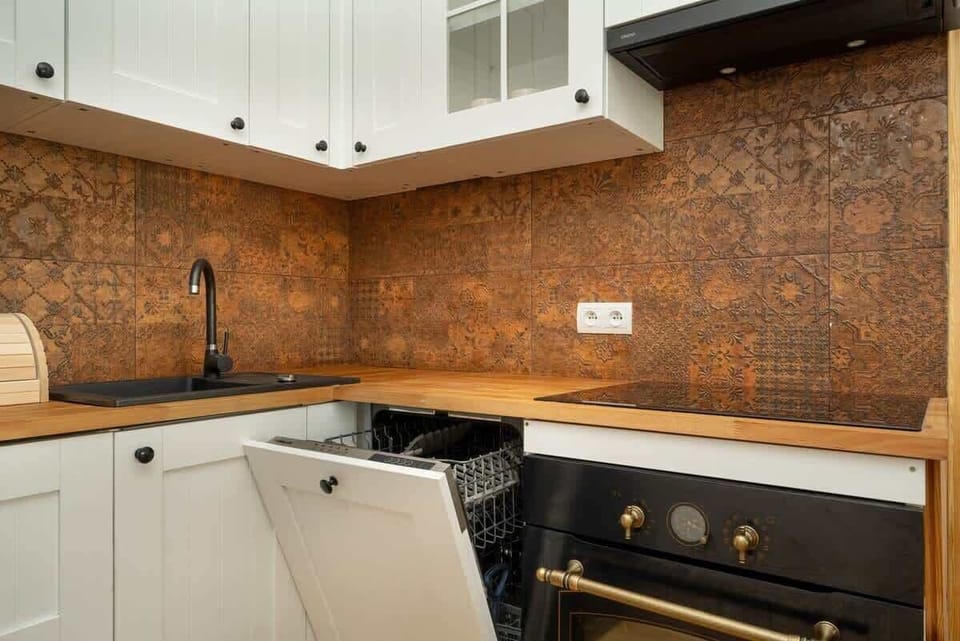 A modern kitchen with white cabinets, a copper backsplash, and a built-in oven.
