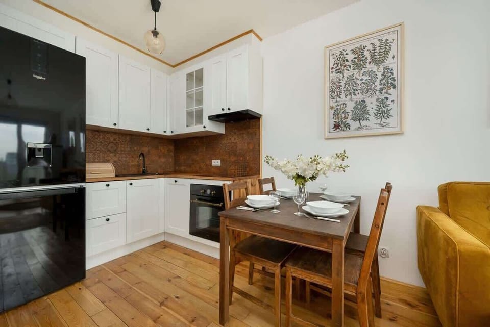 A modern kitchen with wooden cabinets, a dining table, and bright white upper cabinetry.
