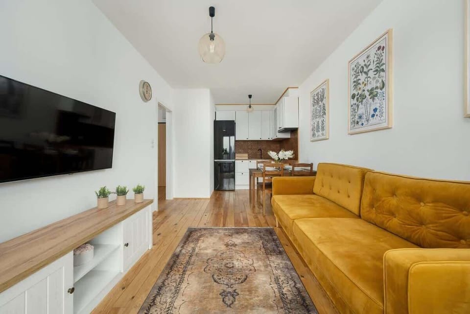 Another view of the living room with the yellow sofa, a TV on a white console, and a glass door leading to the balcony.
