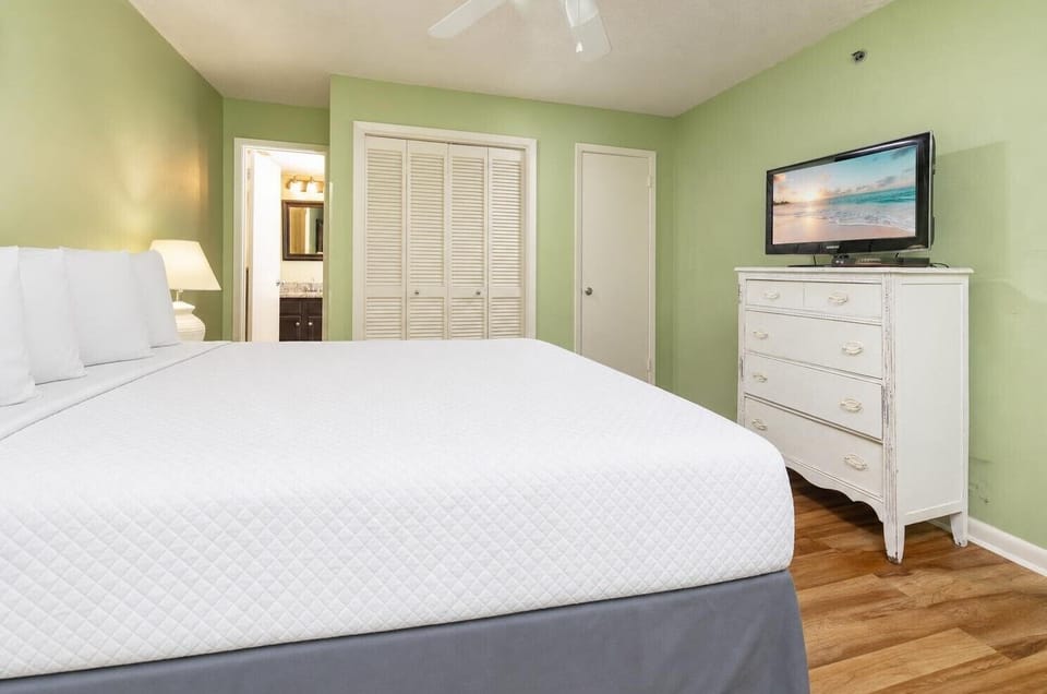This guest bedroom features a comfortable queen bed, a TV for entertainment, and a calming green color scheme