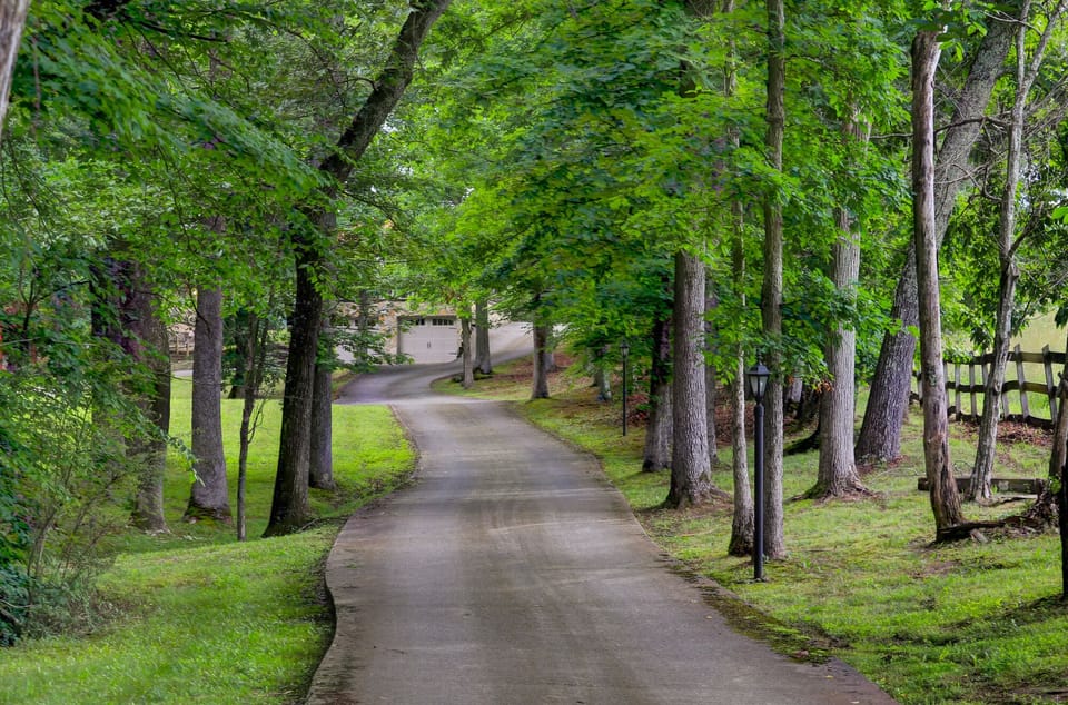 Private driveway, manicured lawns, tall oaks, and maple trees on rolling hills.