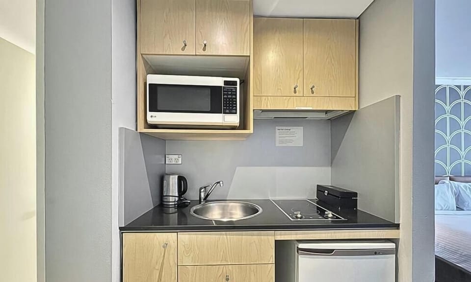 Kitchenette with microwave, bar fridge, cooktop, and cabinetry.