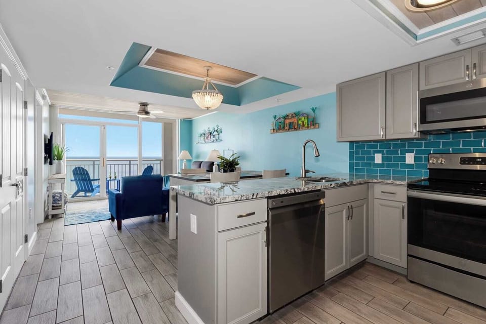 Cook and entertain in style with this open-concept kitchen featuring sleek stainless steel appliances, granite countertops, and vibrant coastal accents. Overlooking the living area and balcony, it's perfect for enjoying meals with ocean views.