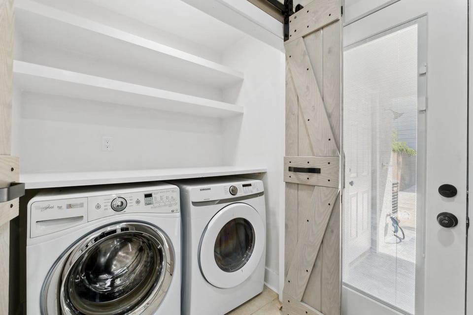 Laundry area with modern washer and dryer behind a rustic sliding barn door.