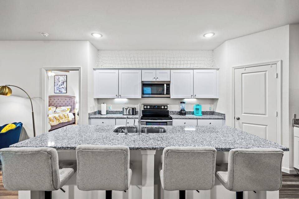 Bright fully stocked kitchen features white cabinetry, granite counters, stainless appliances and breakfast bar seating—ideal for home-cooked meals during construction projects, corporate travel, relocation or insurance stays in Lavon.