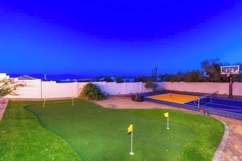 Expansive outdoor recreation area featuring a private basketball court, putting green, and volleyball setup, all set against a stunning twilight sky.