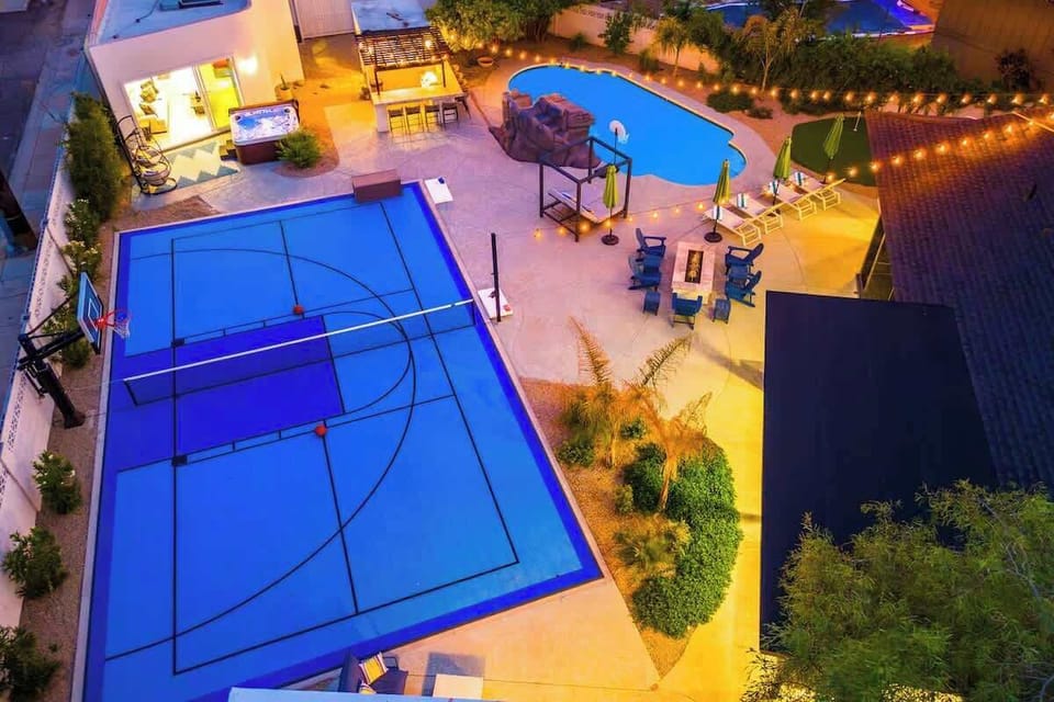 Aerial view of the property showcasing a private basketball court, outdoor swimming pool, covered patio, and beautifully landscaped grounds illuminated at night.
