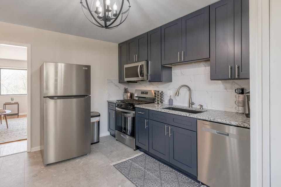 Sleek, fully updated kitchen with modern gray cabinetry, stainless steel appliances, and marble-style backsplash. Includes dishwasher, microwave, coffee station, and full-size fridge…perfect for home-cooked meals or quick bites.