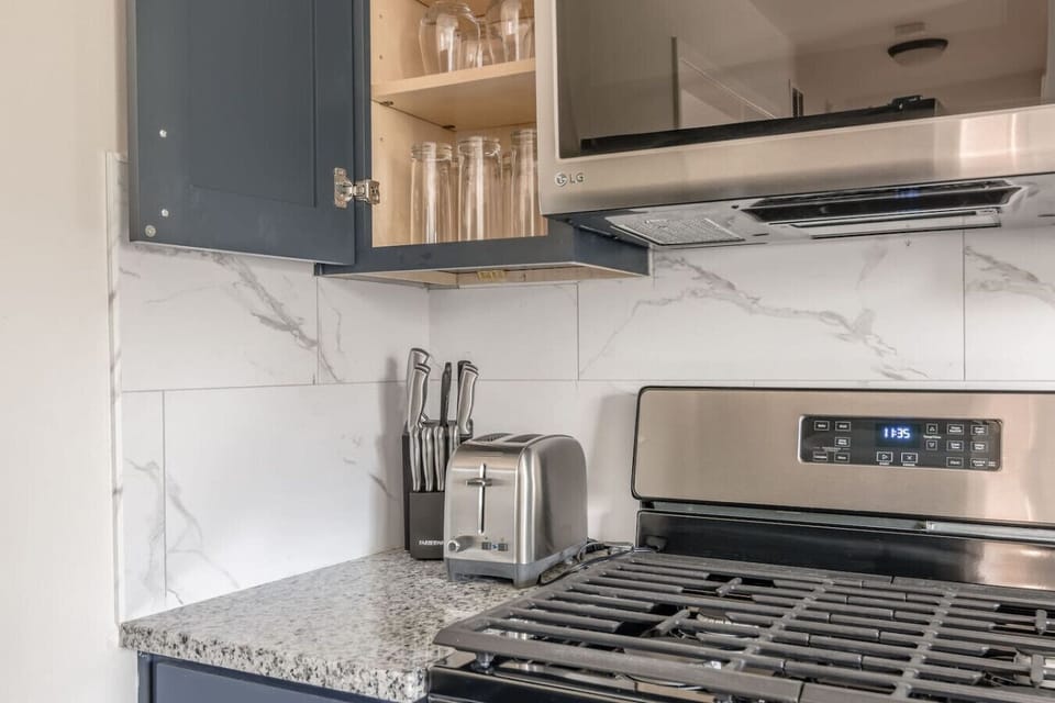 Sleek, fully updated kitchen with modern gray cabinetry, stainless steel appliances, and marble-style backsplash. Includes dishwasher, microwave, coffee station, and full-size fridge…perfect for home-cooked meals or quick bites.