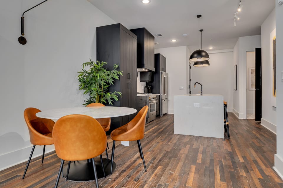 Open dining & kitchen layout w/ round table, warm wood floors & greenery