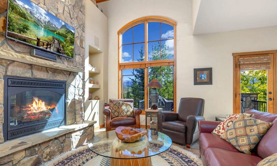 Experience Mountain serenity in our inviting living room, featuring a roaring fireplace and stunning views of the sky through multiple windows.