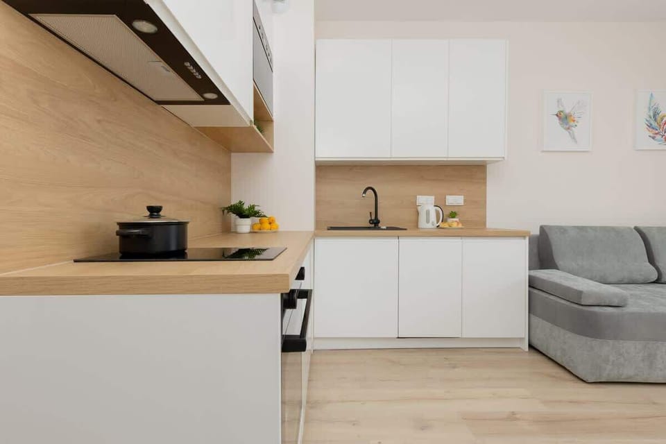 A sleek kitchen with white cabinets, a wooden countertop, and a grey sofa nearby.
