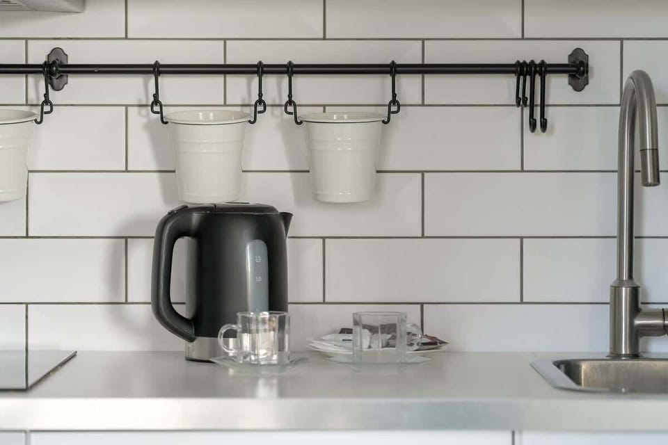 A modern kitchen detail: white subway tiles, a black kettle on the counter, and two mugs hanging on a rail.
