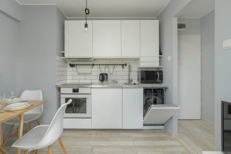 A bright white kitchen with a built-in oven, tiled backsplash, and a compact wooden dining area.
