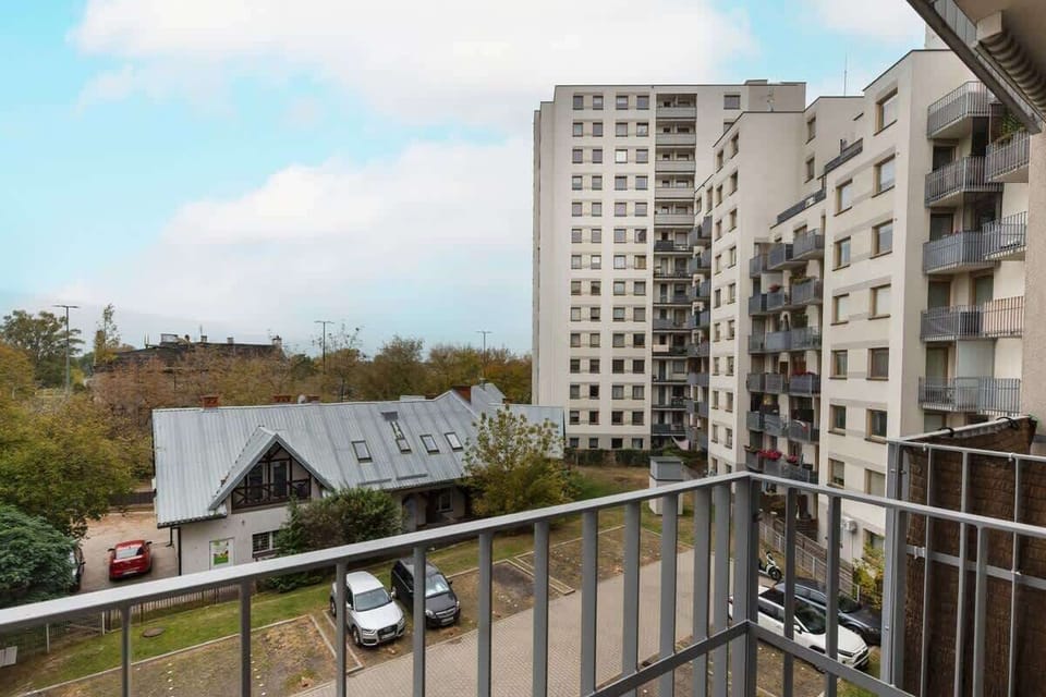 A balcony view overlooking a residential area with modern apartment buildings and trees.
